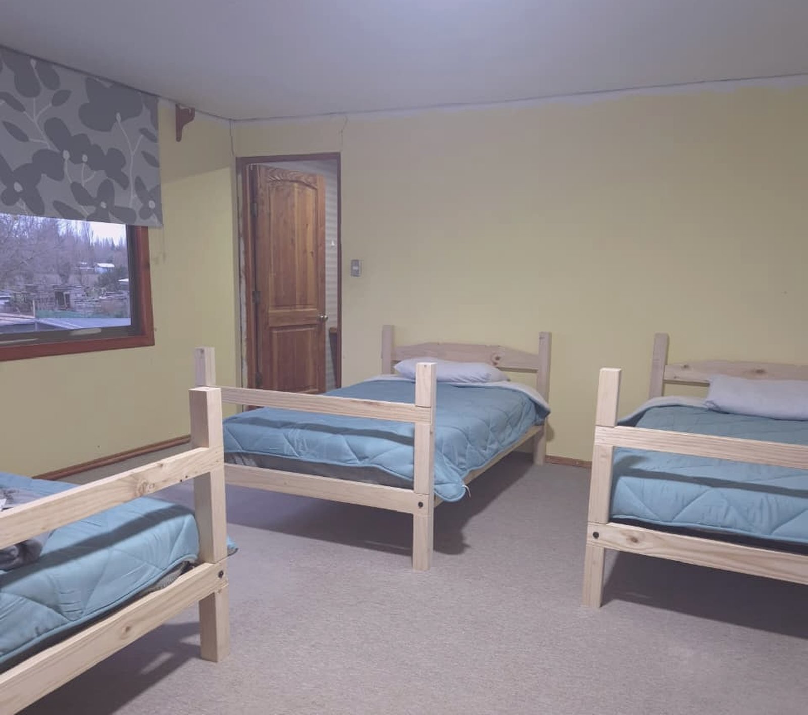Dormitorio compartido de Centro Imperial, con camas individuales de madera y ventana al campo